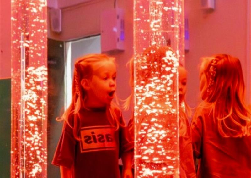 A young girl looking at a red tube with bubbles in it